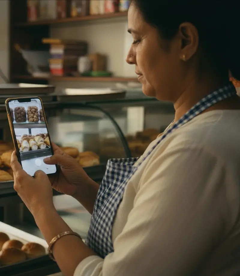 A baker in her shop looking at a phone that shows photos of fresh buns