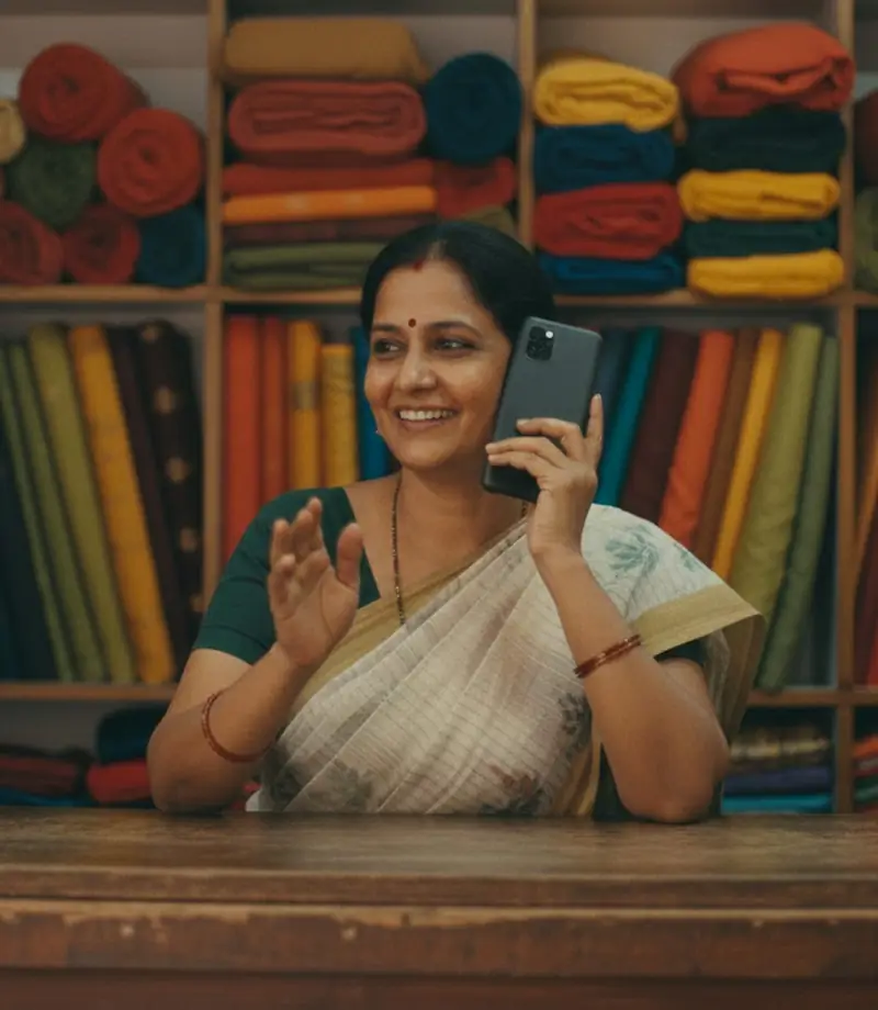 A shop owner among shelves of fabric, smiling as she talks on her phone